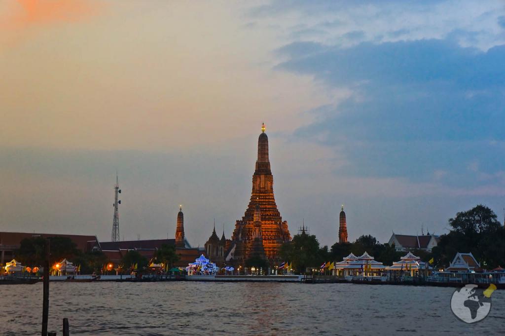 Templo Wat Arun iluminado ao entardecer, visto da margem oposta do rio Chao Phraya.