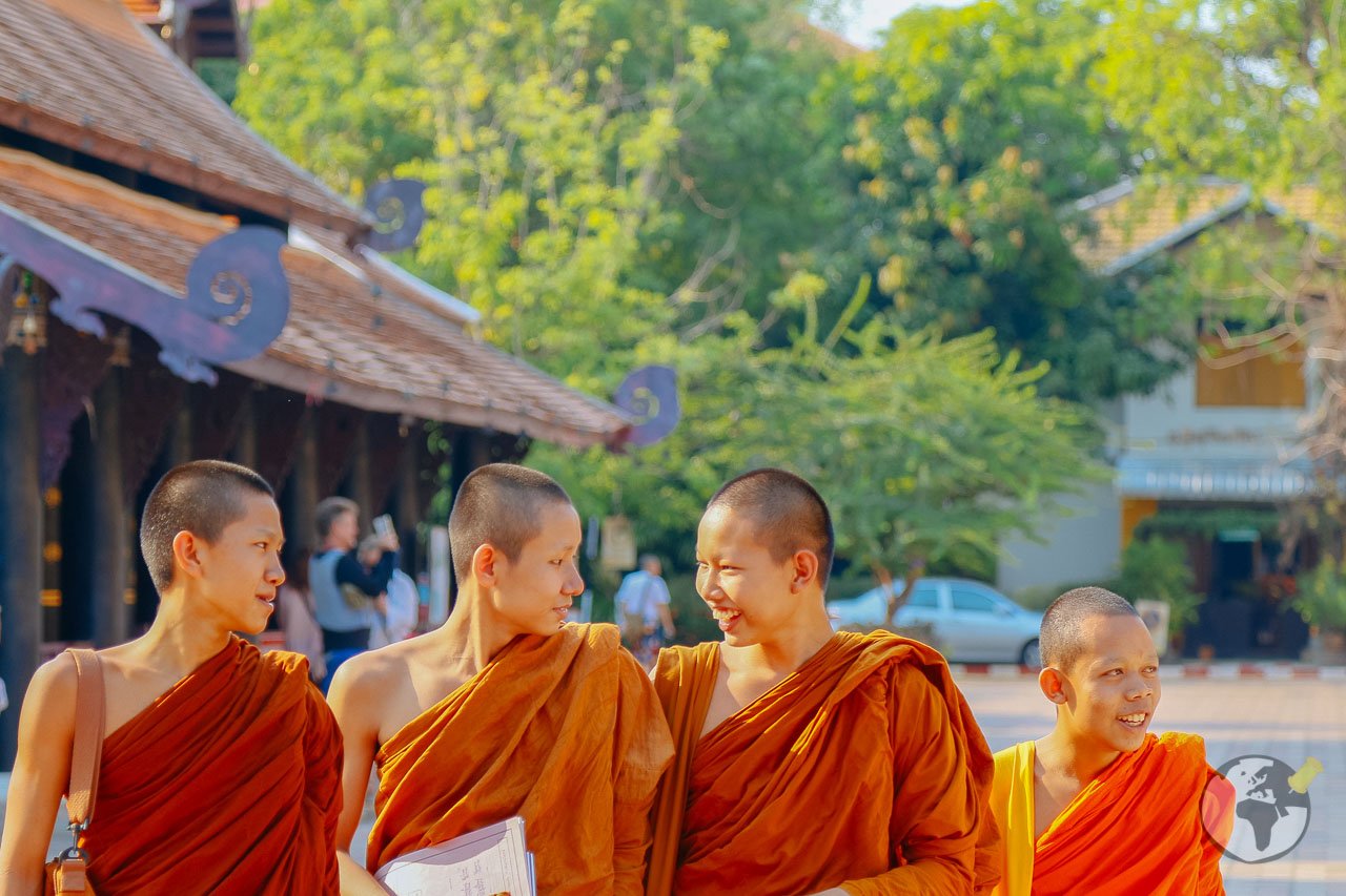 Quatro monges jovens com túnicas alaranjadas caminhando juntos e sorrindo ao ar livre.