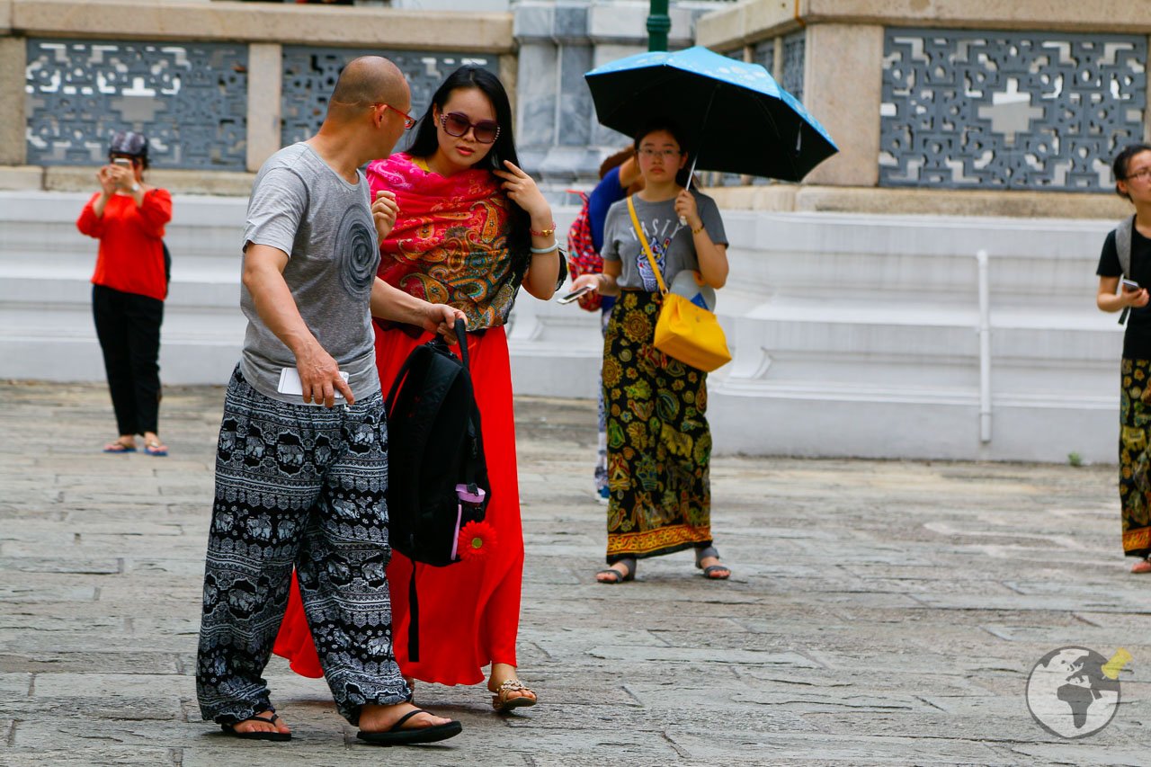 Turistas com roupas cobrindo pernas e ombros circulando por templo na Tailândia.