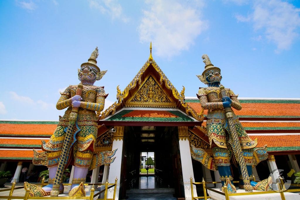 Entrada do Grand Palace em Bangkok com duas estátuas gigantes de guardiões tailandeses ao lado do portão dourado.