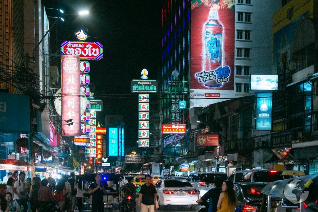 Rua movimentada de Chinatown em Bangkok iluminada por letreiros neon durante a noite.