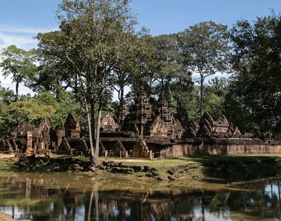 Templo de Banteay Srei cercado por árvores e refletido nas águas de um pequeno lago em Siem Reap.