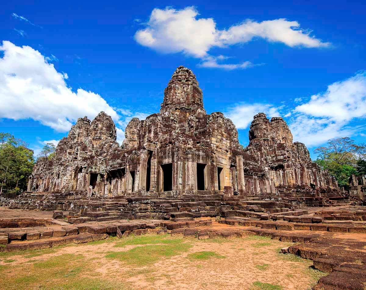 Fachada do templo Bayon em Angkor Thom, com torres esculpidas em pedra sob o céu azul.