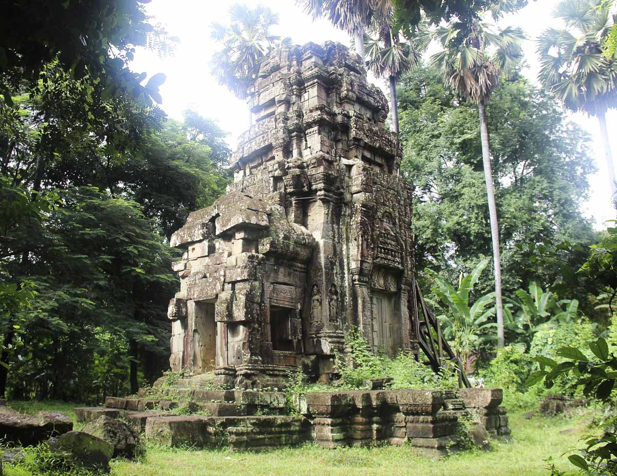 Pequeno templo Ta Prohm Kel cercado por vegetação tropical e palmeiras.