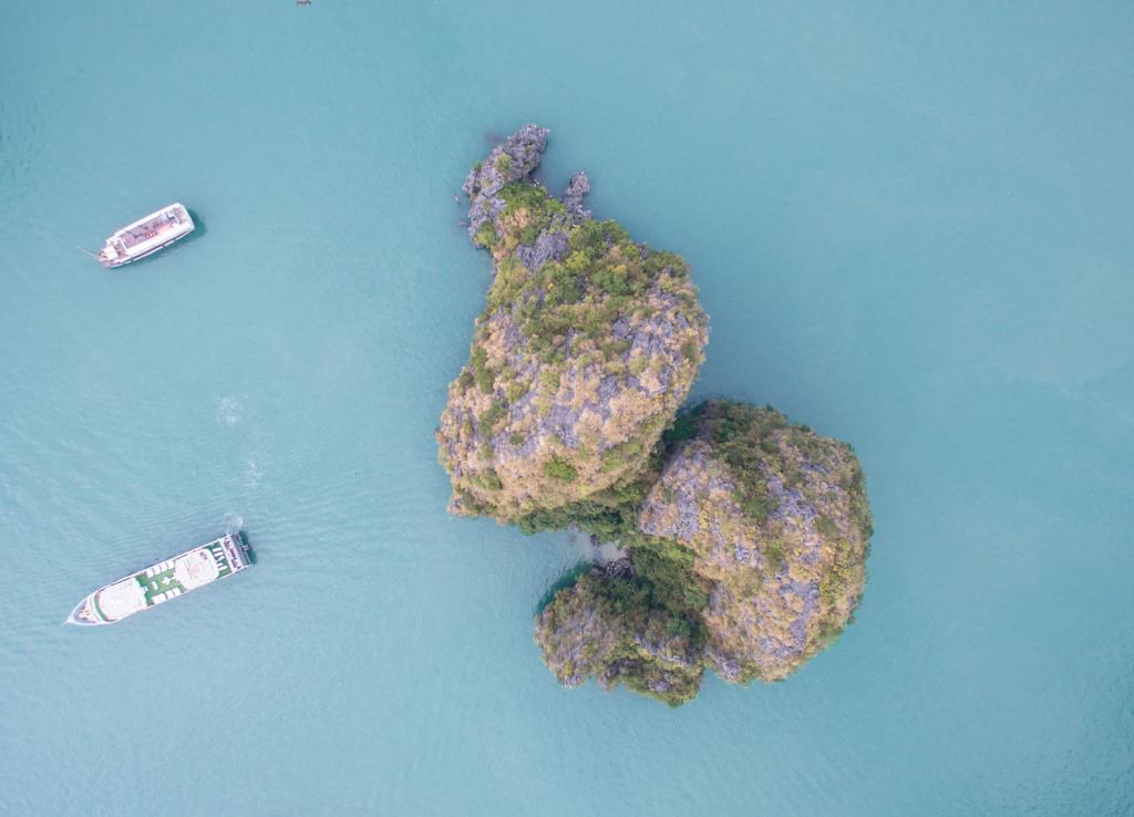 Vista aérea da Luom Bo Area com ilhotas rochosas cobertas de vegetação em meio ao mar azul-claro.