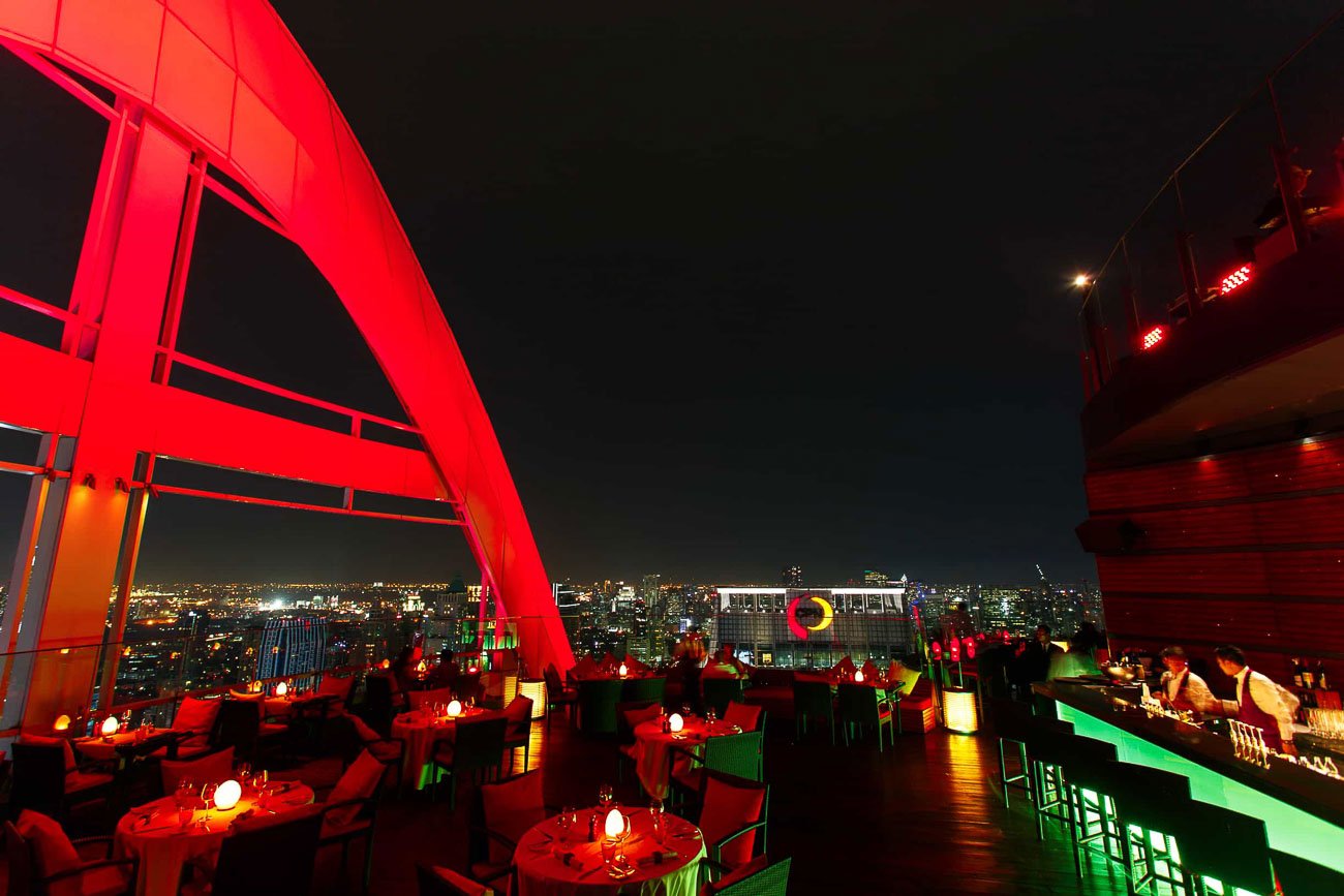 Ambiente sofisticado do Red Sky Bar à noite, com mesas à luz baixa, bar iluminado e arco vermelho marcante.