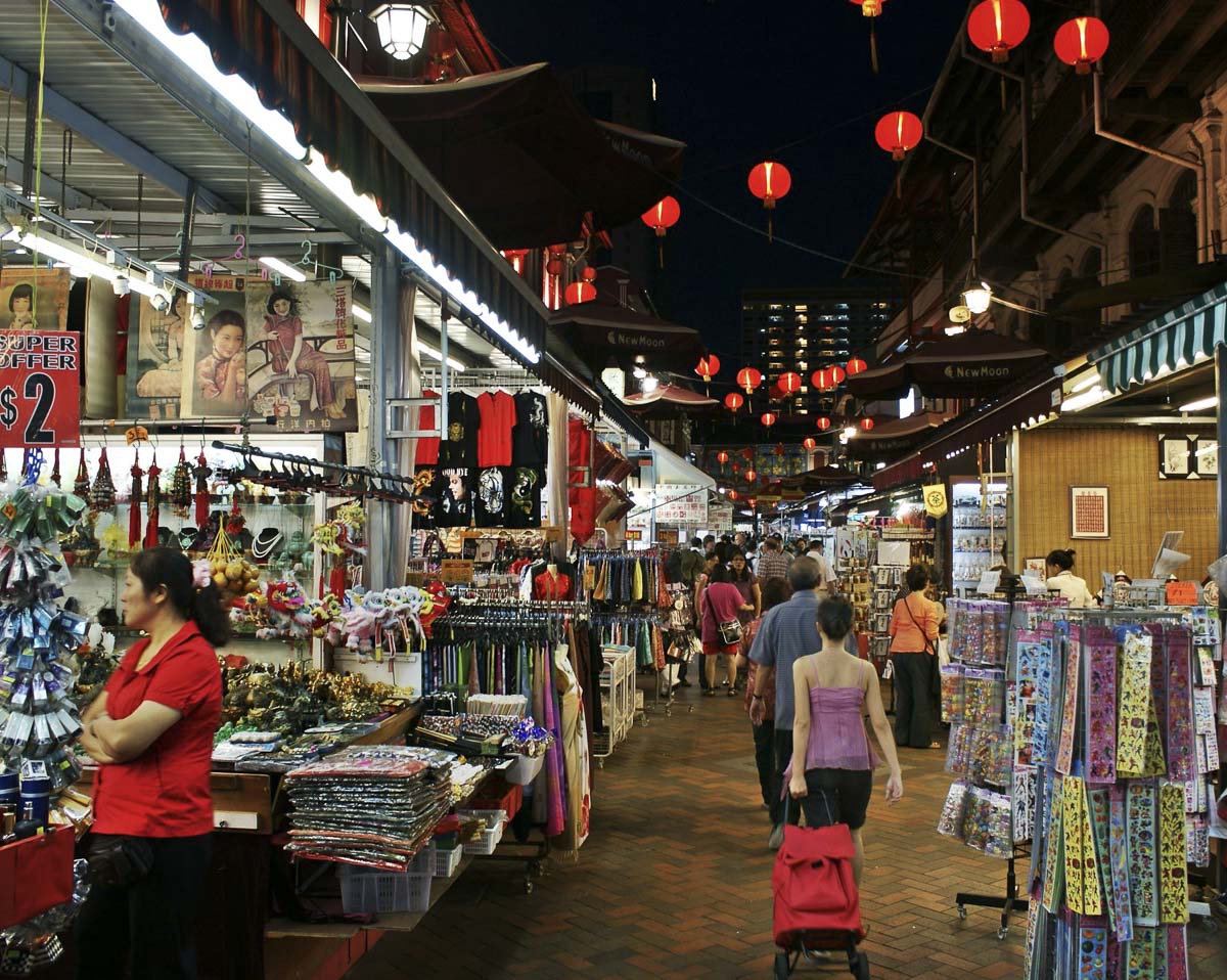 Rua movimentada de Chinatown em Singapura, com lojas e lanternas vermelhas penduradas.