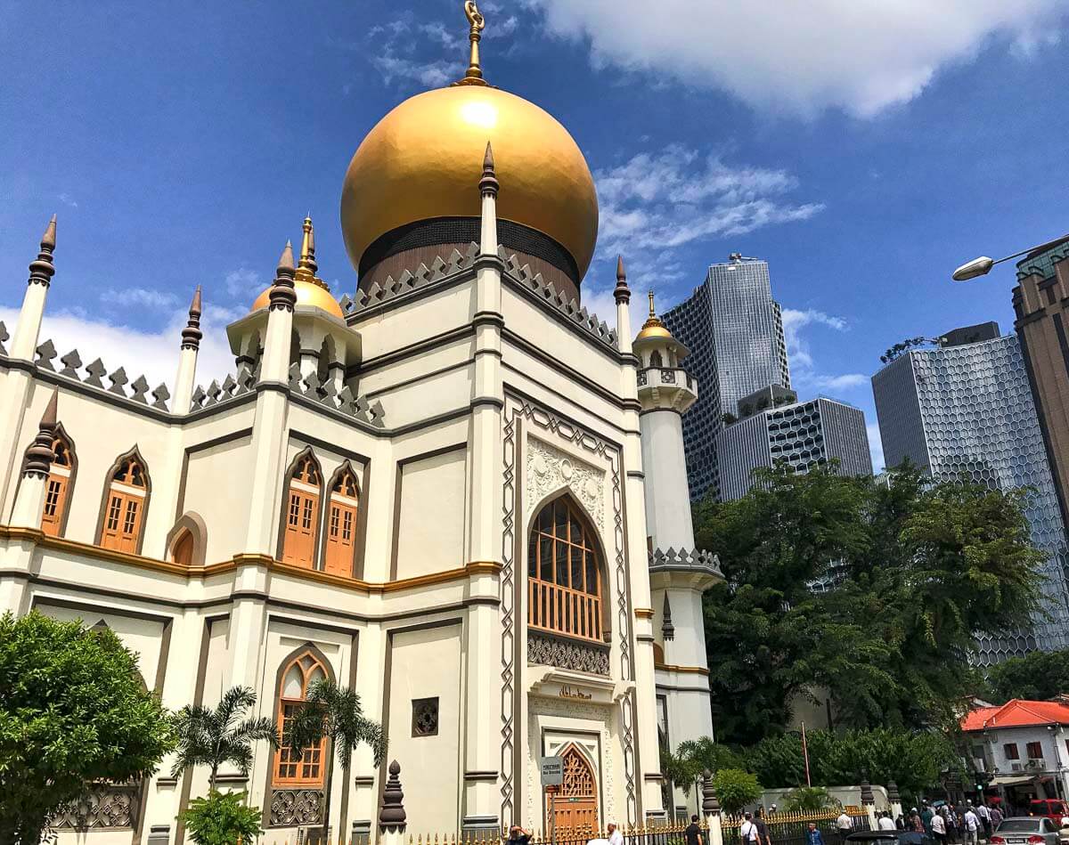 Fachada branca e dourada da Sultan Mosque, com cúpula dourada brilhando sob o céu azul em Singapura.