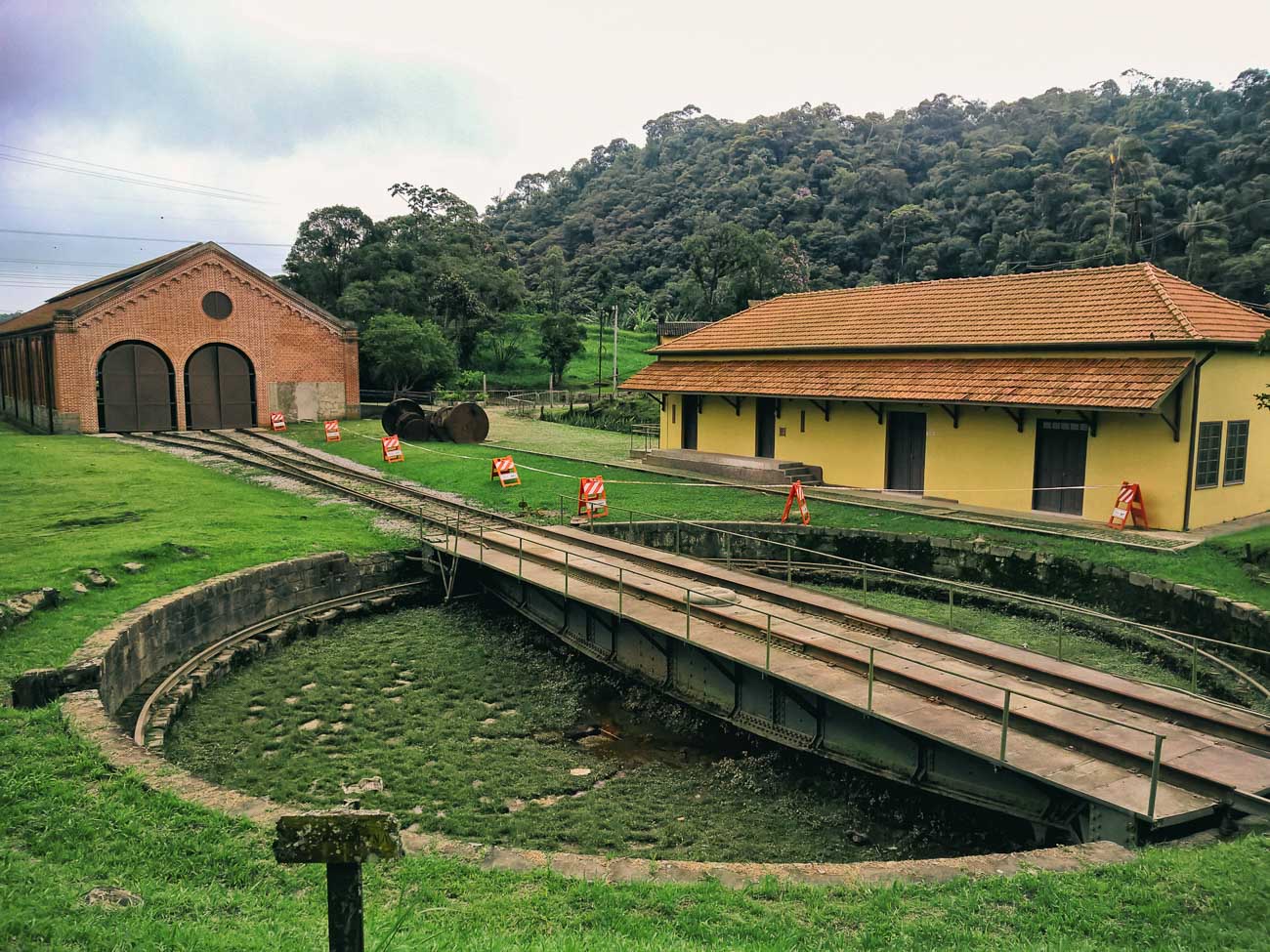 Pátio da estação ferroviária de Paranapiacaba, com área gramada e montanhas ao fundo