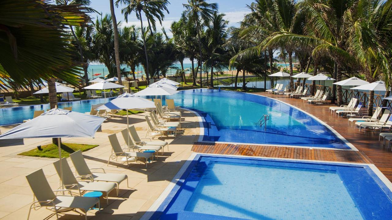 Grande piscina ao ar livre cercada por coqueiros em resort em Maceió