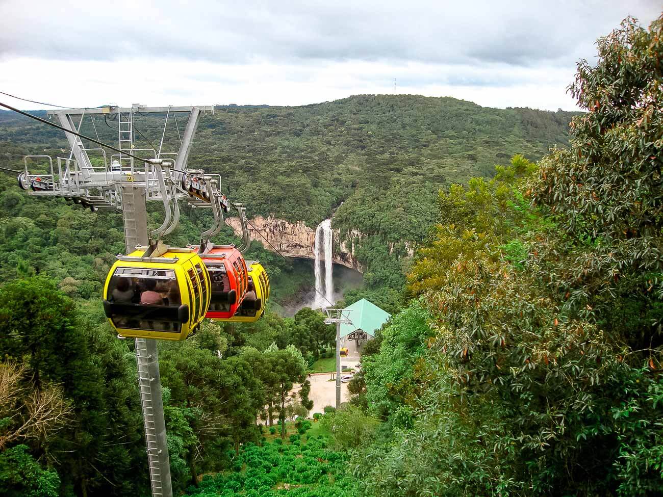 Bondinhos aéreos coloridos atravessando o Parques da Serra e ao fundo a Cascata do Caracol