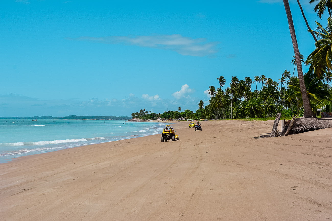 Praia de Antunes com extensa faixa de areia, orla com vegetação e buggy pela areia