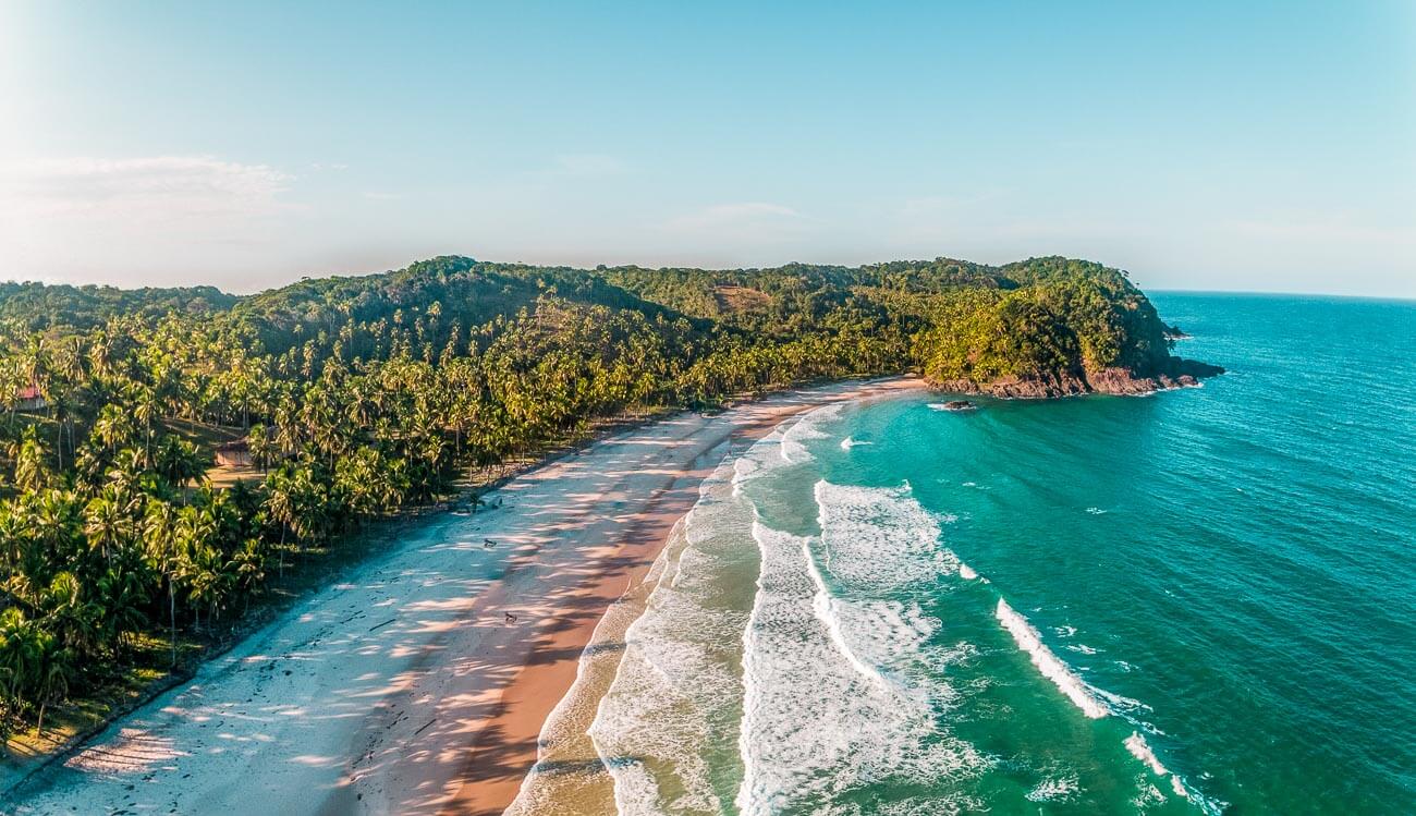 Prainha com o mar em tons de azuis e rodeada pela natureza