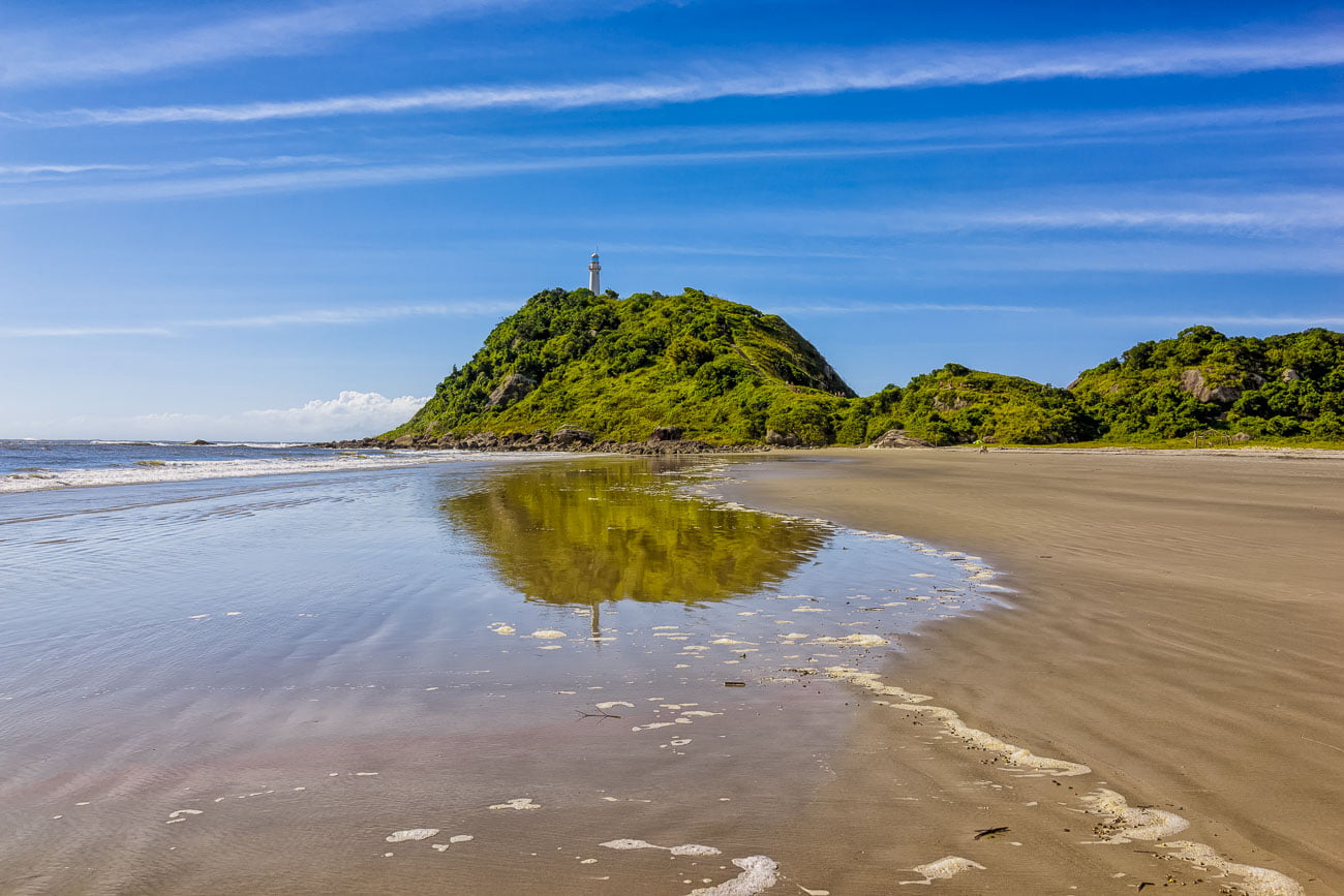 Faixa de areia e ao fundo morro com o Farol das Conchas