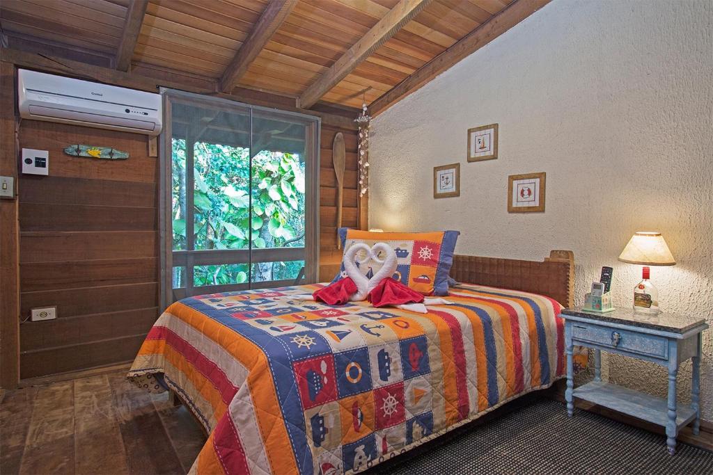 Quarto com cama de casal com manta colorida e móveis rústicos em pousada na Ilha do Mel