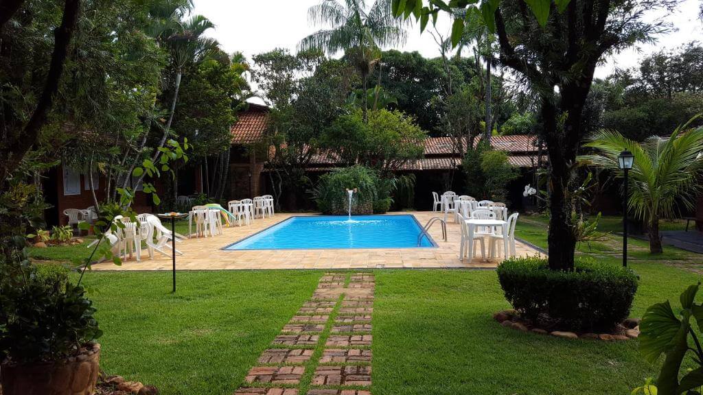 Piscina ao ar livre em área gramada e arborizada com mesas e cadeiras