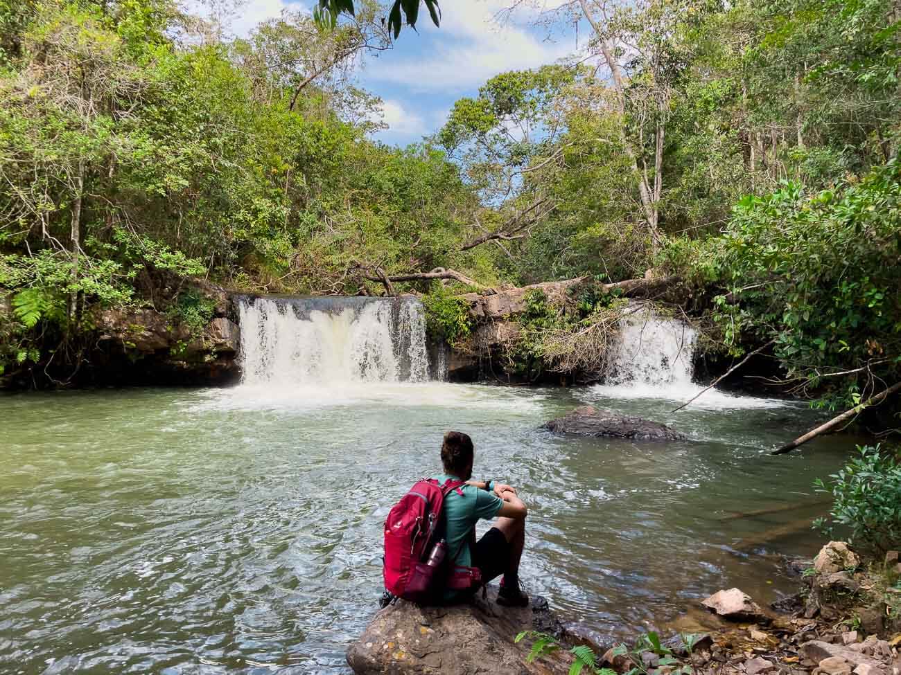 Homem sentado em pedra na beira do poço da Cascata da Anta