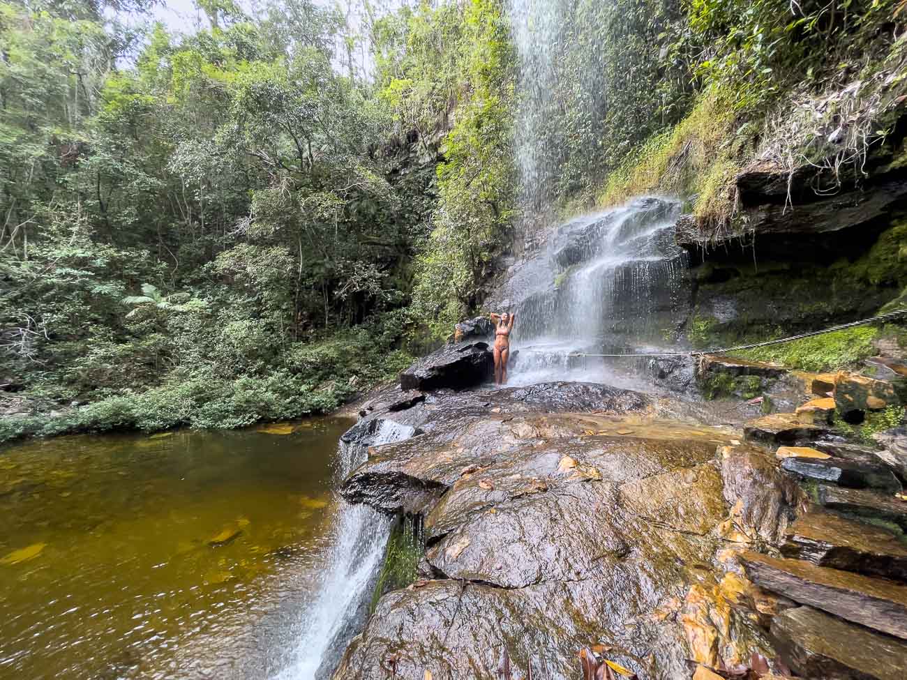 Mulher embaixo da queda d'água da Cachoeira do Rosário em Pirenópolis