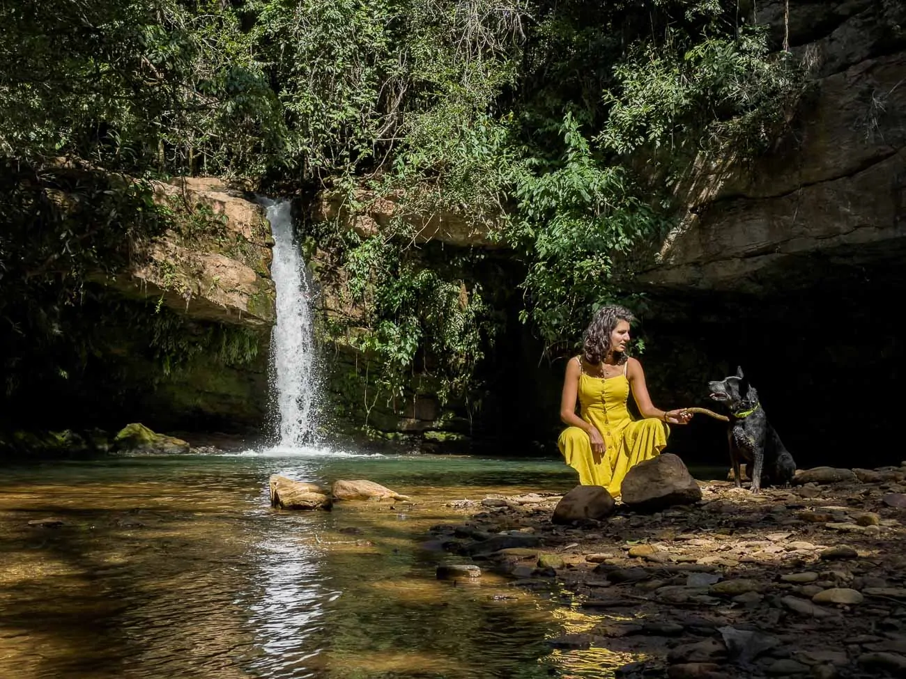 Mulher sentada em pedra brincando com um cachorro na Cachoeira do Sileno