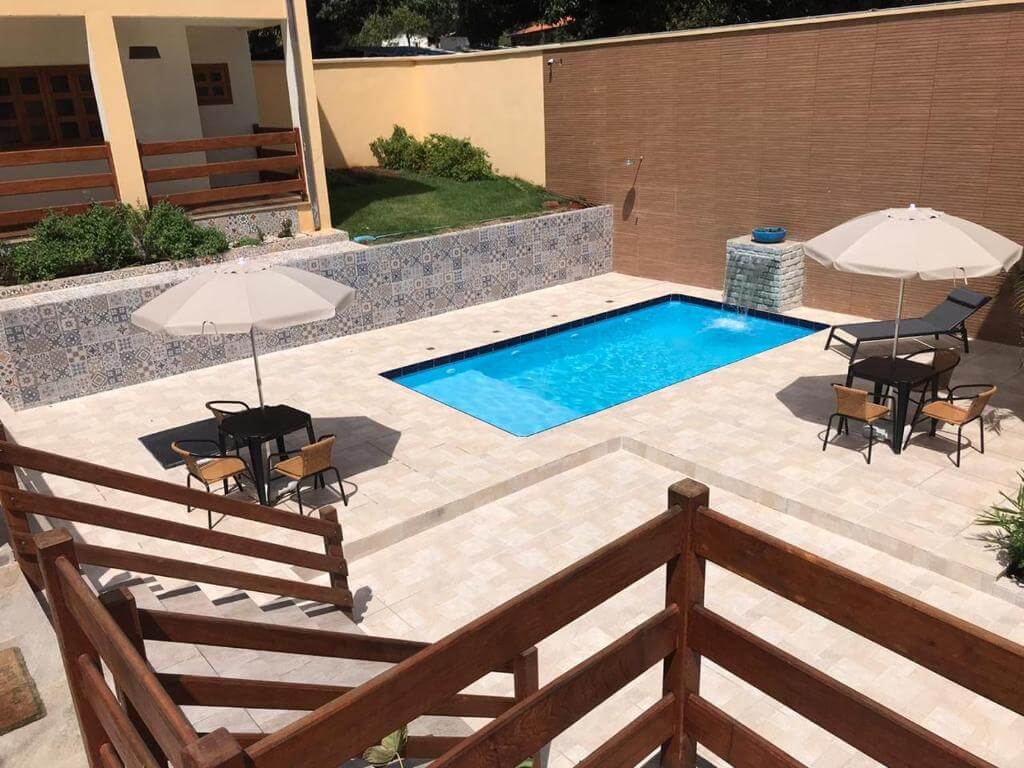 Piscina ao ar livre, com mesas, cadeiras e guada-sóis na borda.
