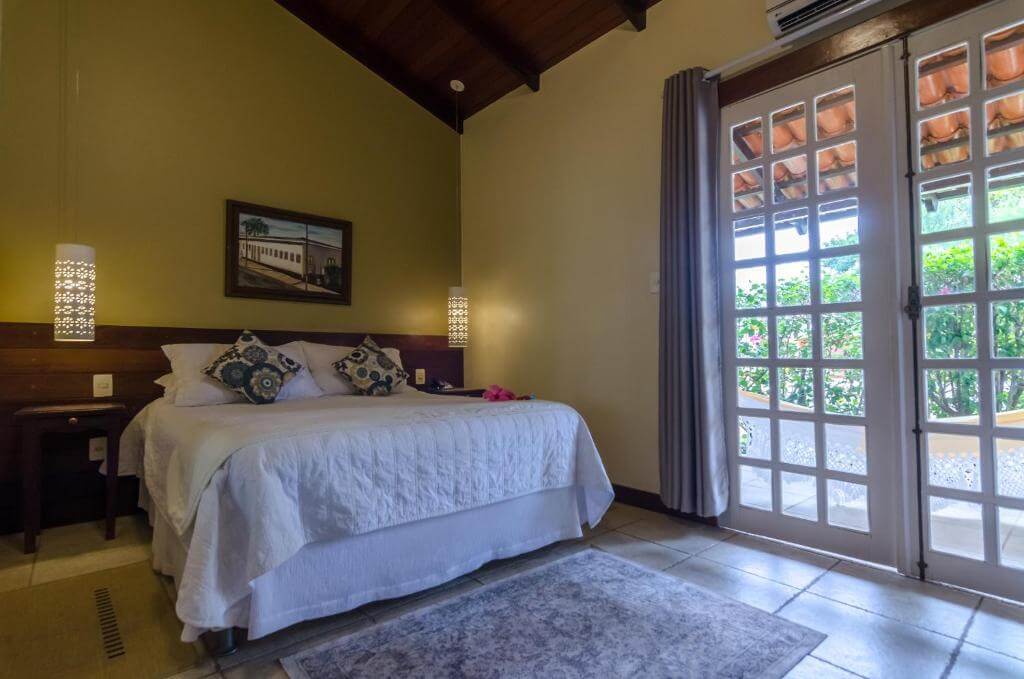 Quarto de casal espaçoso com porta de vidro com vista para área externa da pousada tajupá