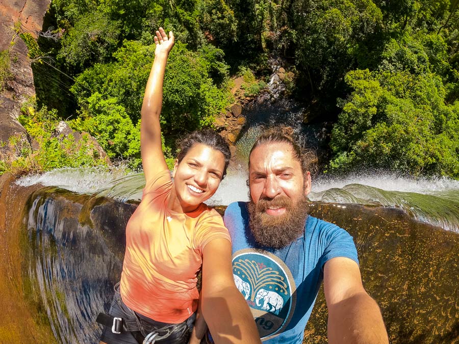 Casal tirando foto enquanto faz ancoragem na Cachoeira da Cortina, inclinados em direção ao poço abaixo.