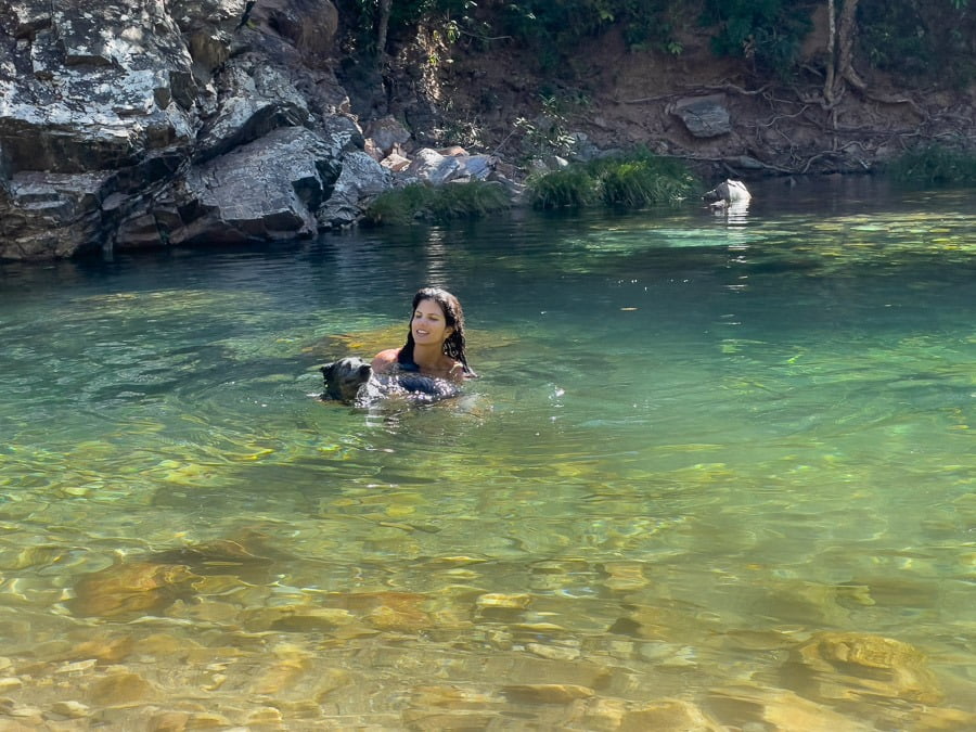 Mulher e cachorro nadando no poço de águas azuis cristalinas da Cachoeira do Segredo