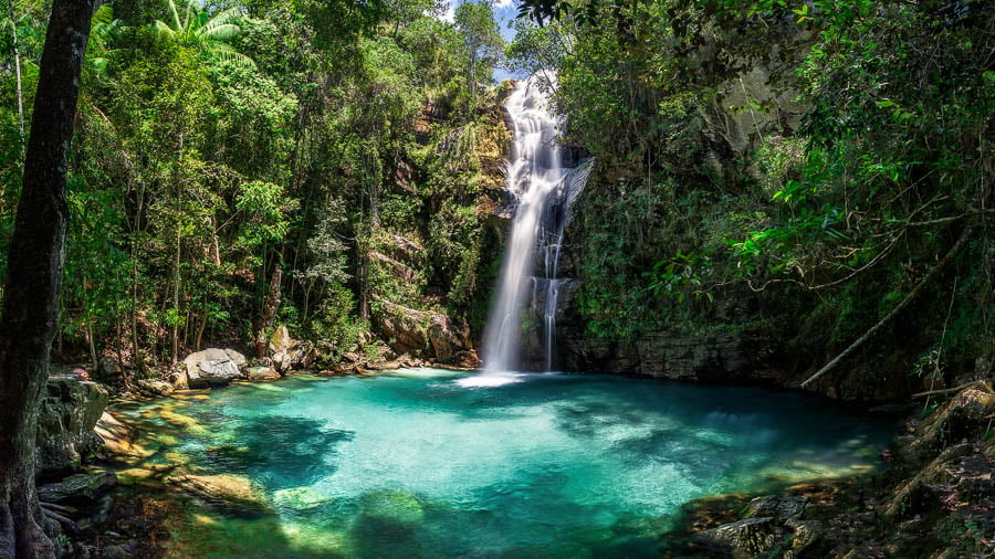 Poço de águas azuis turquesas e queda d'água ao fundo rodeada pela natureza na Cachoeira Santa Bárbara