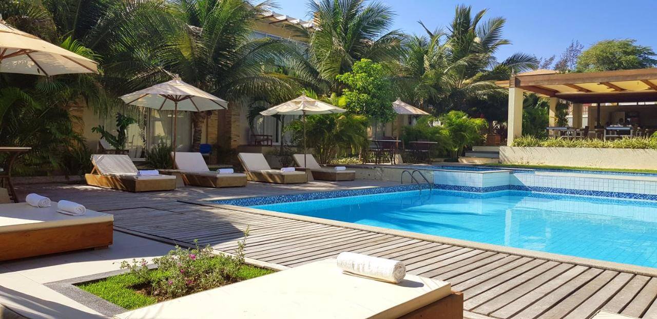 Piscina ao ar livre em área com coqueiros, espreguiçadeiras e guarda-sóis