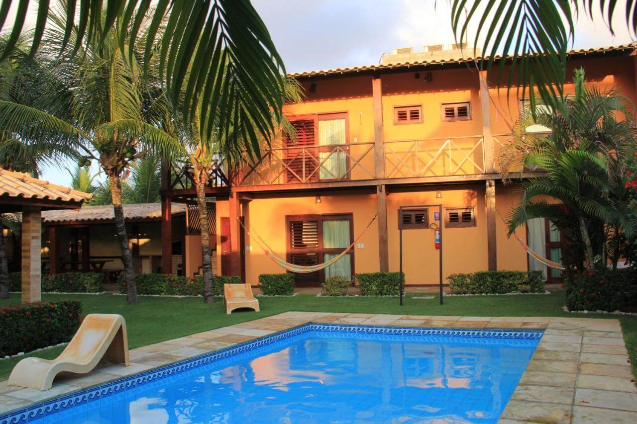 Piscina ao entardecer e ao fundo pousada em Cumbuco