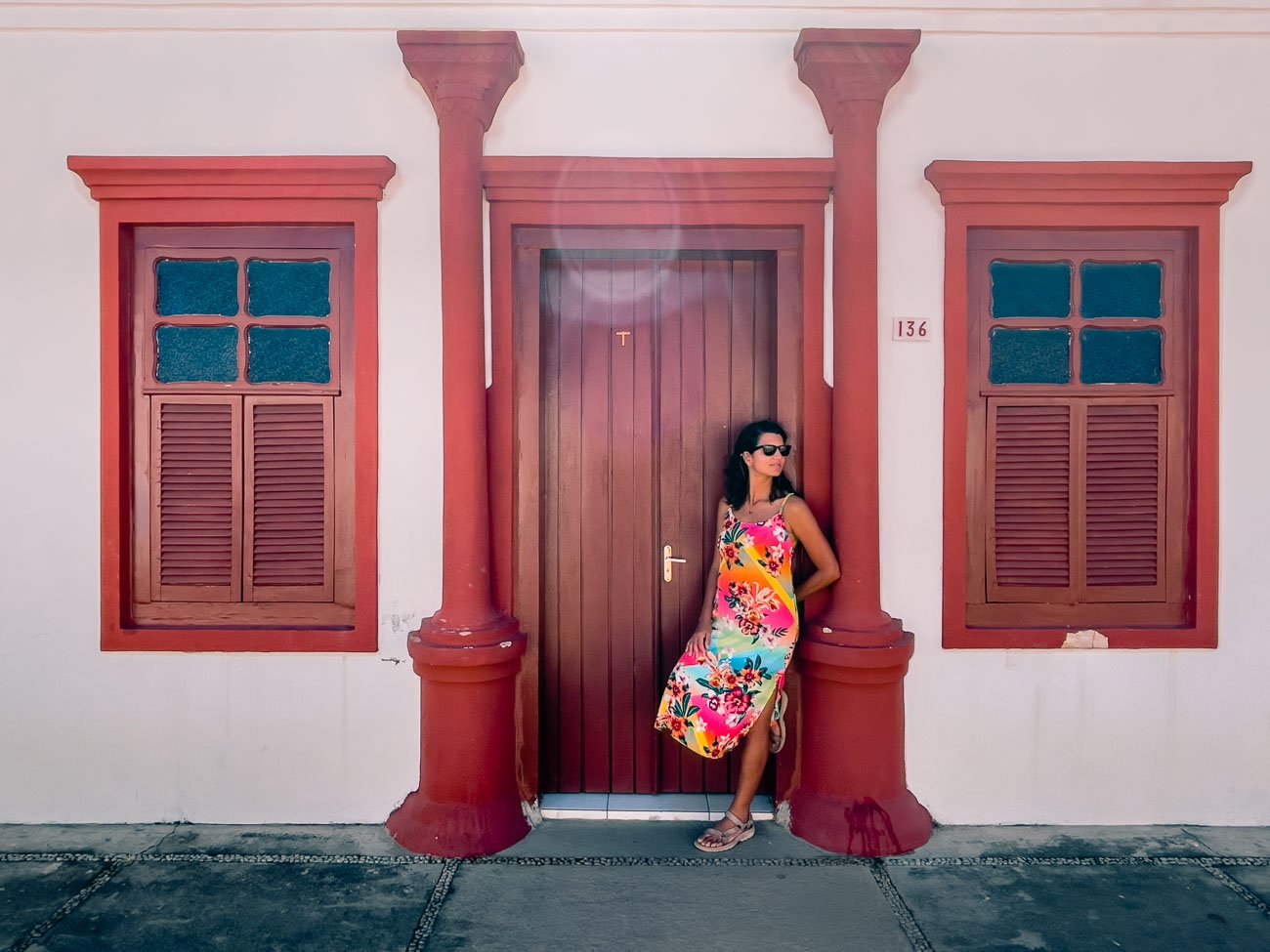 Mulher em pé apoiada em porta vermelha de construção colonial no Centro Histórico de Natividade