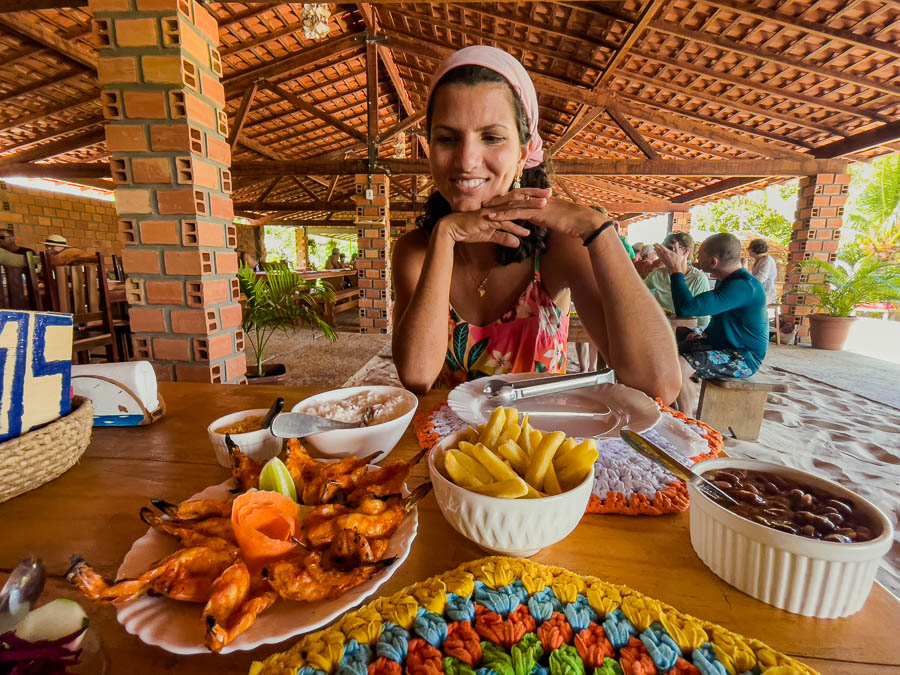 Mulher sentada com as mãos apoiando o queixo olhando para uma mesa com camarões fritos e batata frita em restaurante nos Lençóis Maranhenses