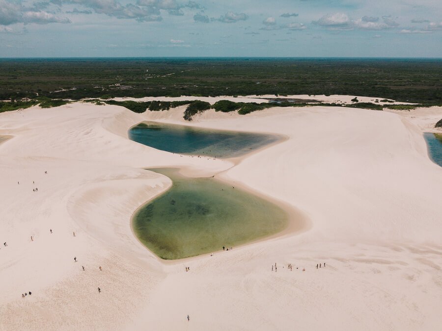Vista de cima da Lagoa da Preguiça nos Lençóis Maranhenses com tons verdes entre as dunas de areia branca.