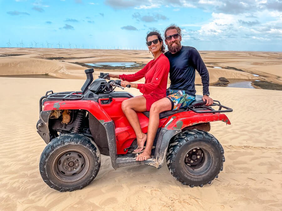 Um homem e uma mulher sentados em um quadriciclo entre as dunas dos Lençóis Maranhenses