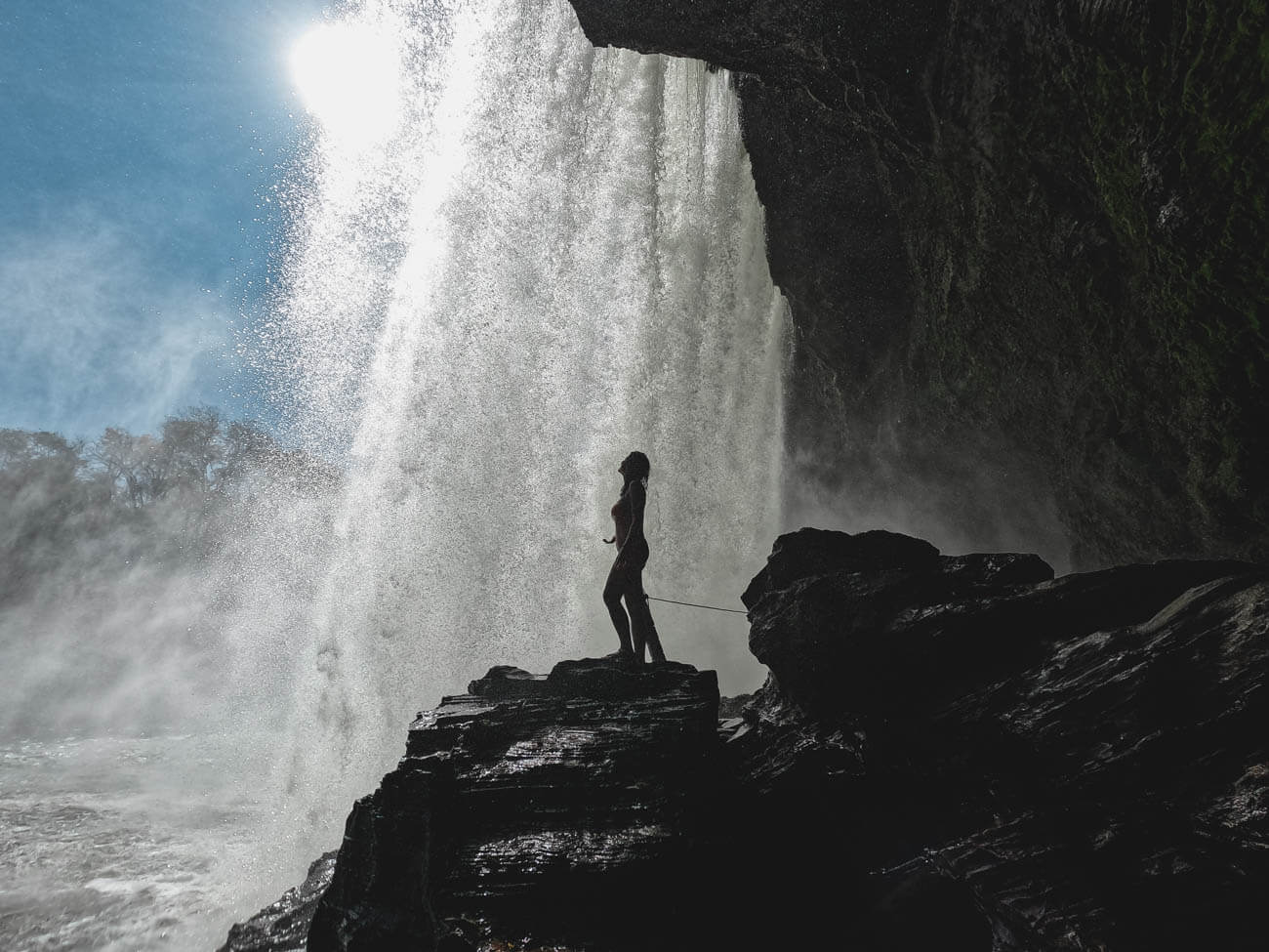 Mulher em pé em uma pedra atrás da queda da Cachoeira São Romão na Chapada das Mesas