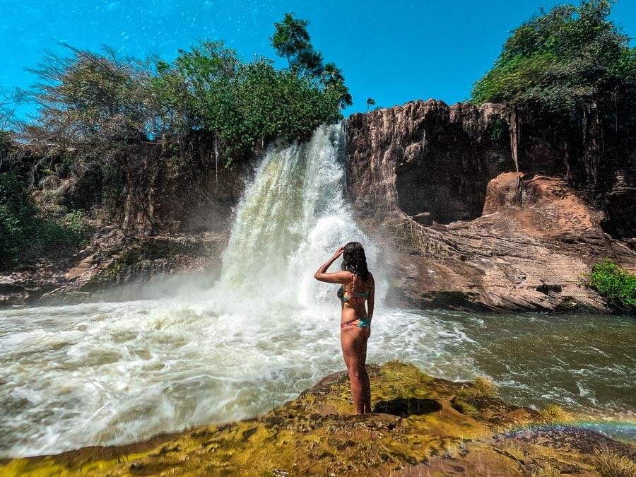 Mulher em pé nas margens do poço da Cachoeira do Prata na Chapada das Mesas e ao fundo queda d'água