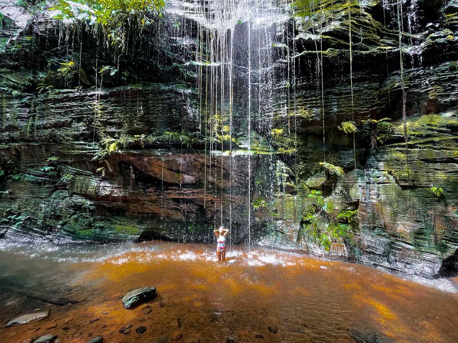 Mulher tomando banho na queda d'água da Cachoeira do Santuário em meio aos paredões na Chapada das Mesas