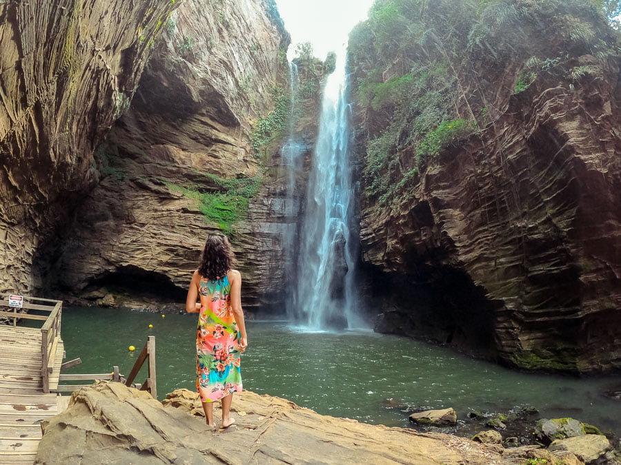 Mulher parada em pedras de frente para o poço e queda d'água da Cachoeira Santa Bárbara
