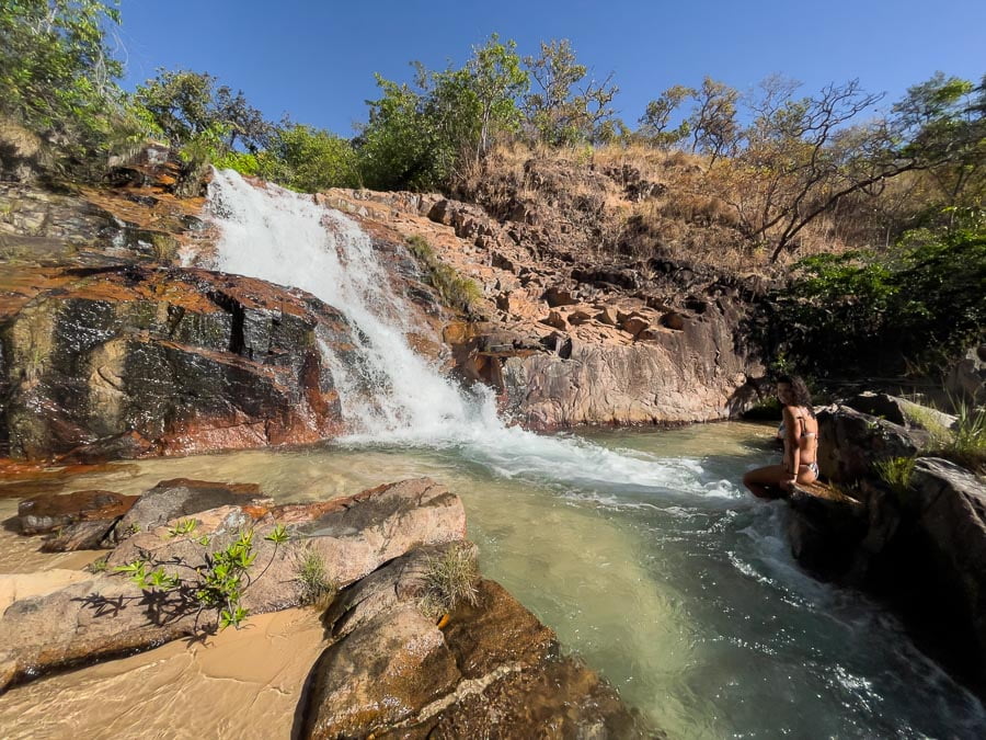 Poço de águas cristalinas e queda d'água da Cachoeira do Sombra em Aurora com uma mulher sentada em uma pedra em frente à queda
