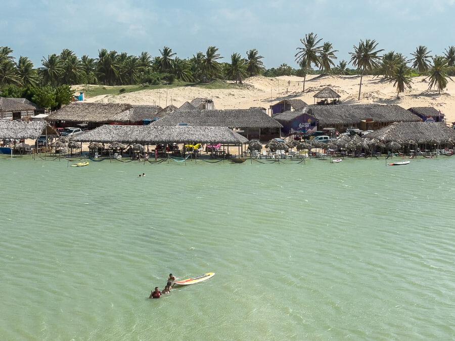 Lago Grande em Camocim com águas claras e cristalinas. Ao fundo redes e restaurantes rústicos próximos à margem e dunas