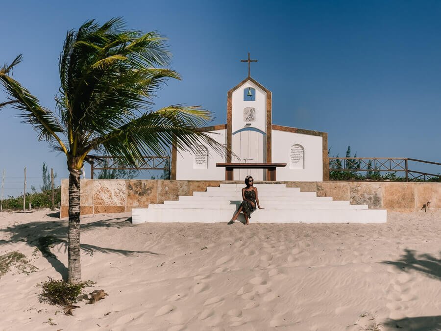 Igreja com pequena escadaria com uma mulher sentada em um dos degraus na Praia de Carnaúbas