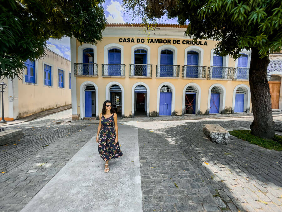 Mulher caminhando em frente à fachada colonial da Casa Tambor de Crioula