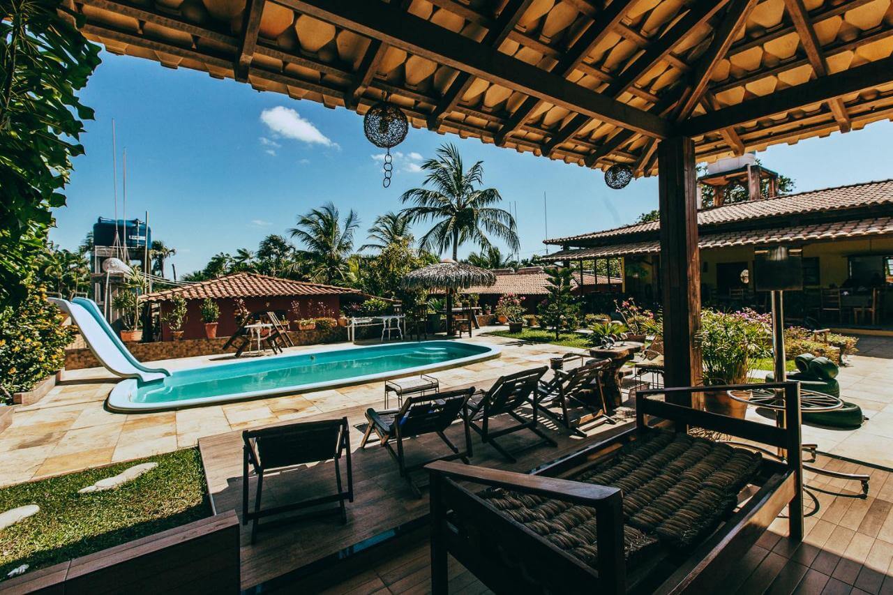 Área externa de pousada com piscina ao ar livre e alguns canteiros de flores 