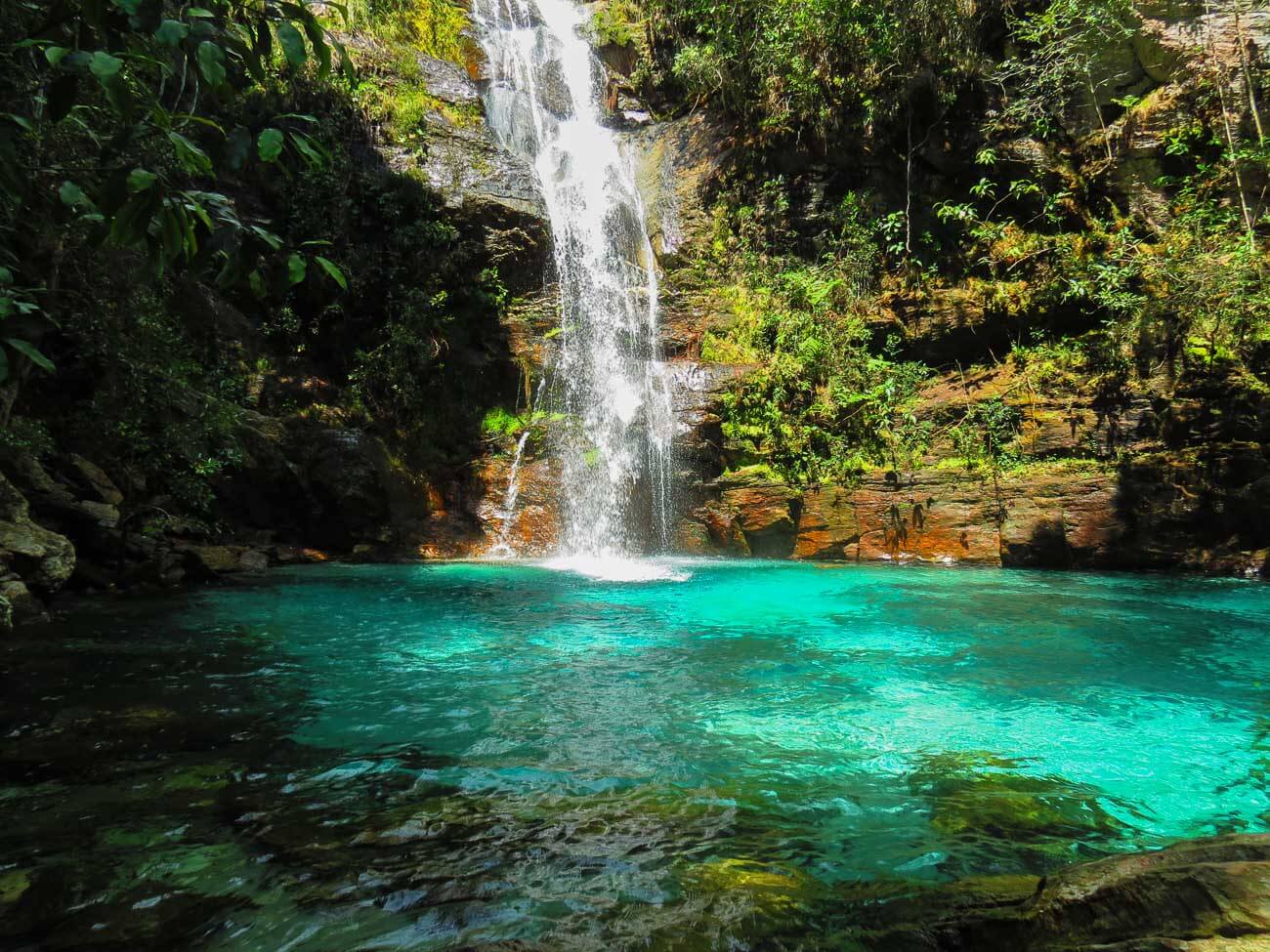 Poço de águas azuis turquesas e queda d'água ao fundo rodeada pela natureza na Cachoeira Santa Bárbara