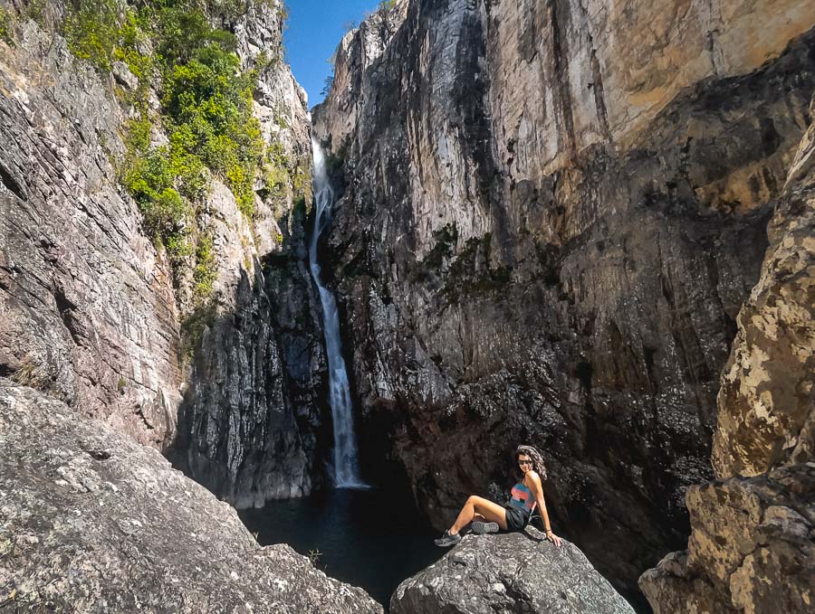 Mulher sentada em uma pedra e ao fundo o poço e queda d´água da Cachoeira Veredas.