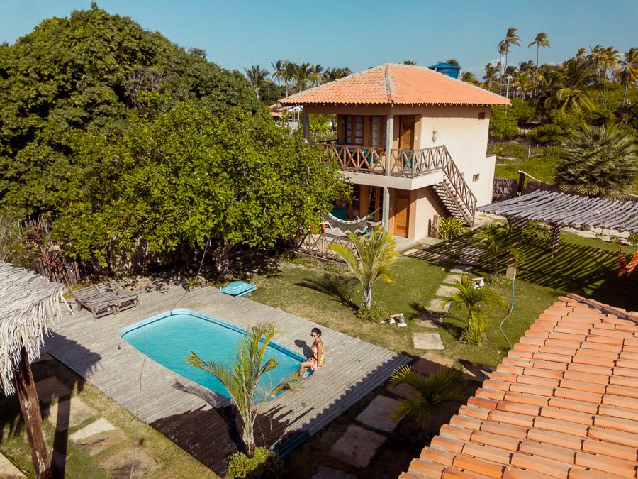Vista de cima de mulher sentada na borda de piscina com os pés na água em pousada em Atins
