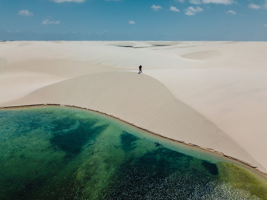 Casal de beijando no topo de uma duna do circuito Lagoa Betânia. Abaixo da duna, uma lagoa em tons verdes.