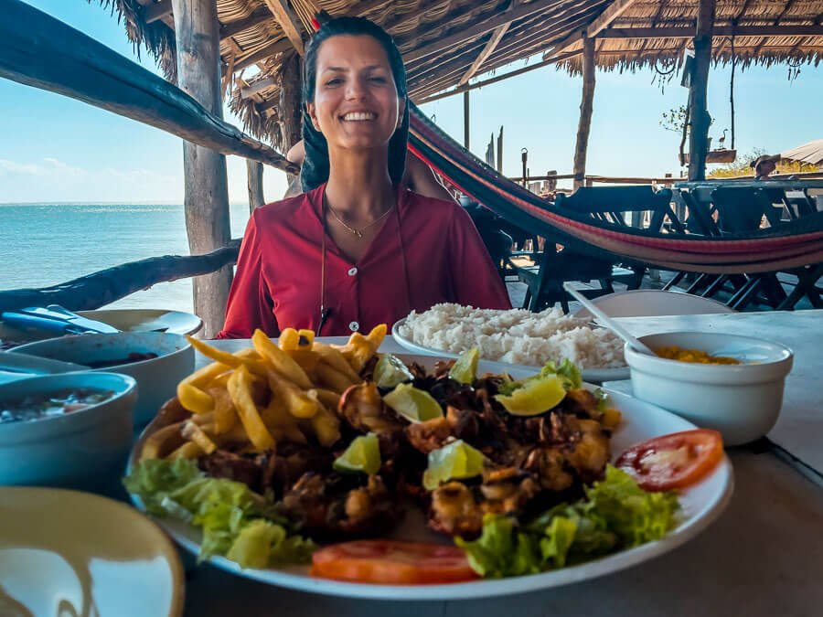 Uma mulher sentada em restaurante à beira mar com um prato de lagostas fritas na mesa