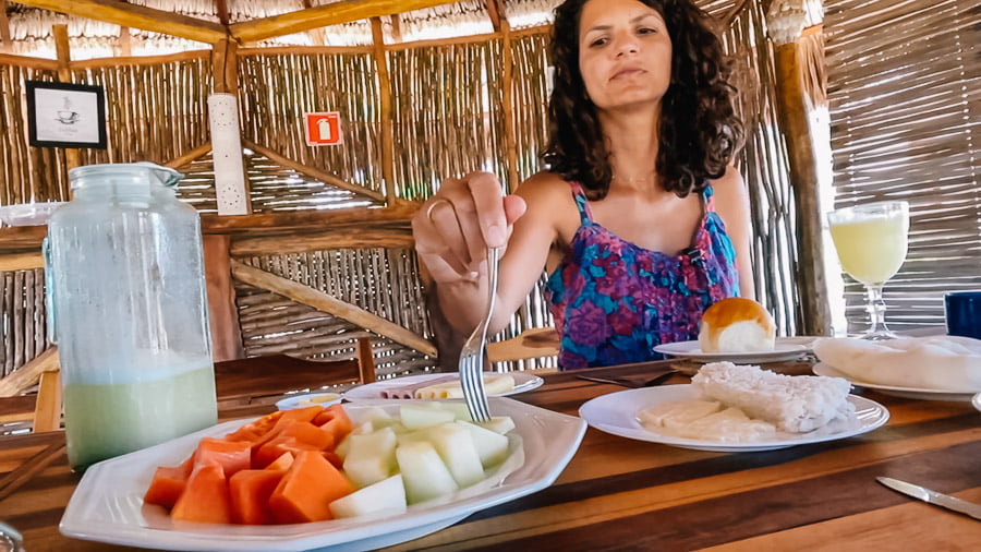 Mulher sentada pegando uma fruta com o garfo durante o café da manhã na Pousada Arecales