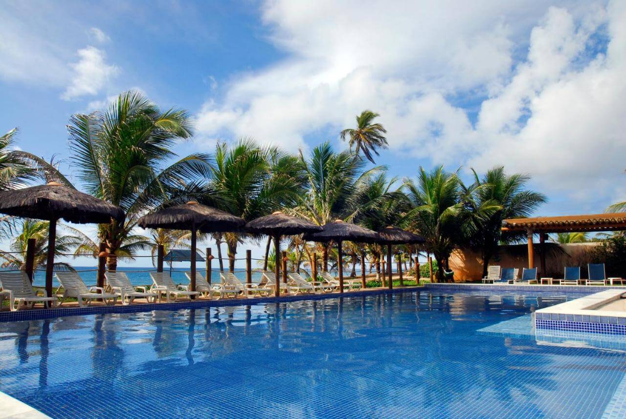 Piscina ao ar livre rodeada por coqueiros e espreguiçadeiras em hotel em Salvador
